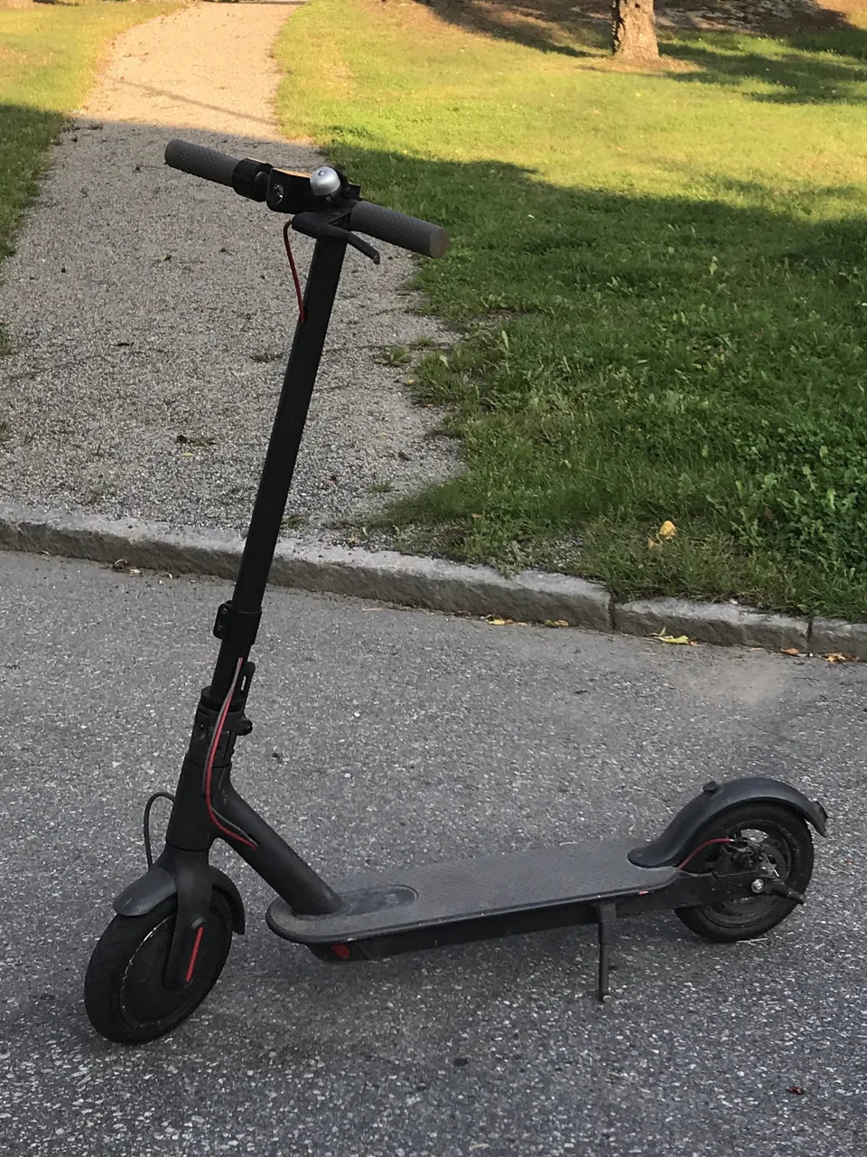 Patinete Xiaomi M365 negro estacionado en un camino junto a césped.