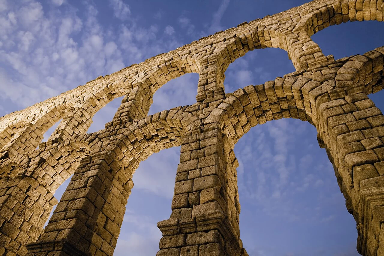 Arcos de granito del acueducto de Segovia iluminados al anochecer, vistos desde abajo.