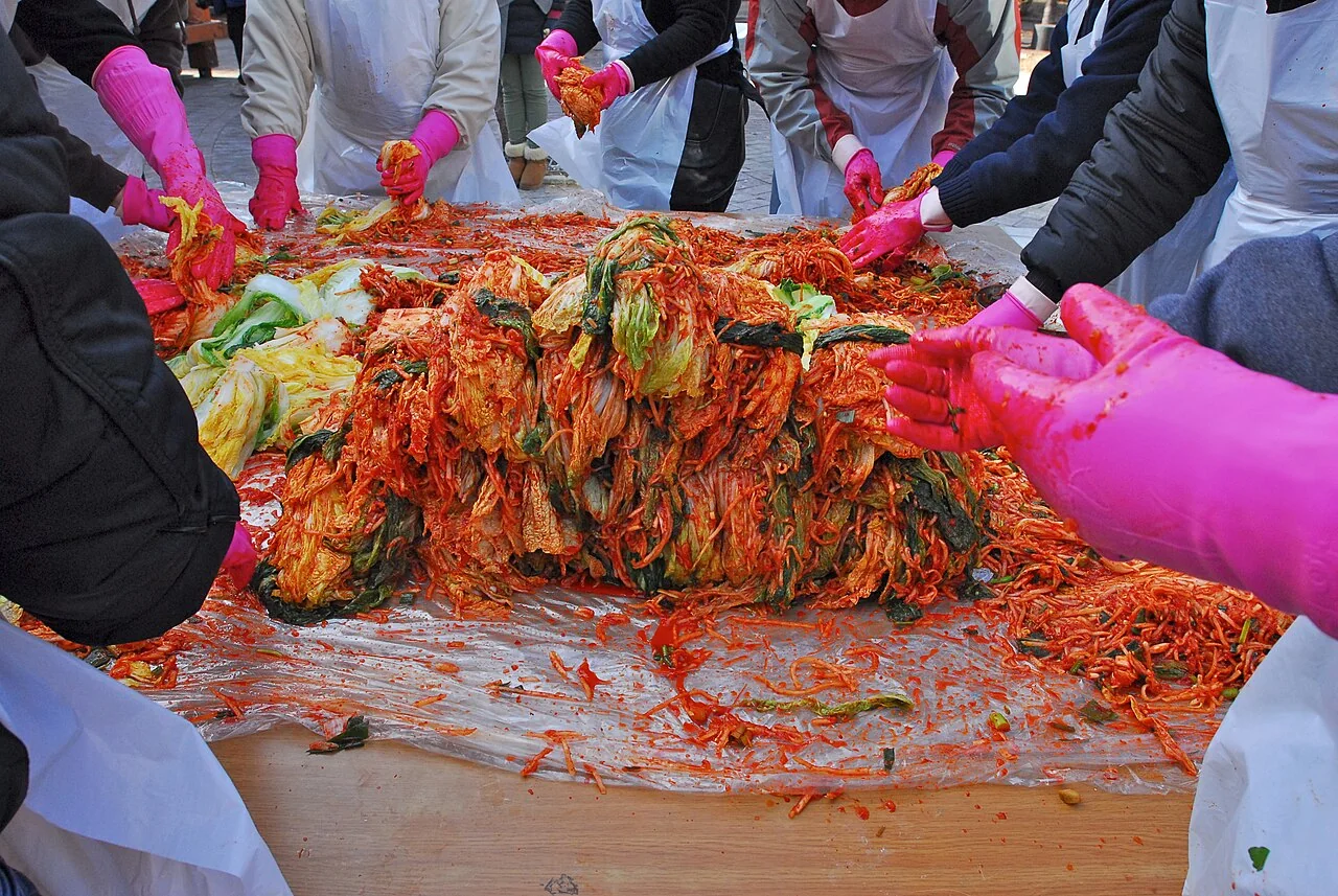 Varias personas preparan kimchi juntas sobre una mesa.