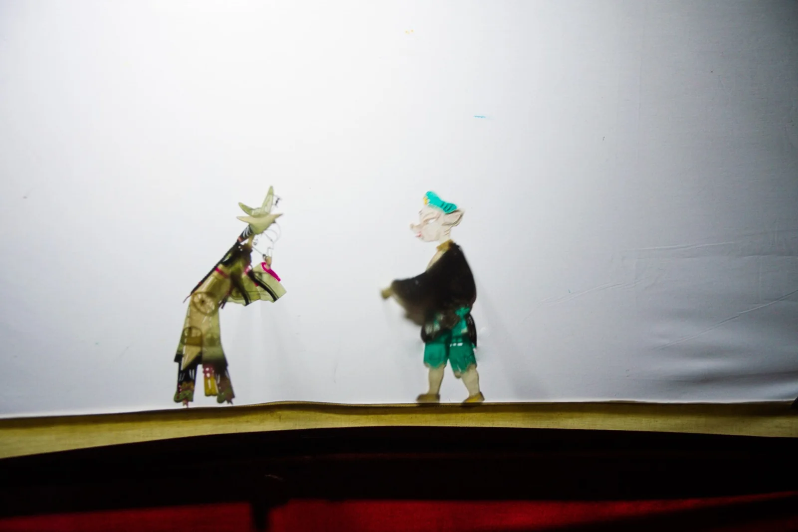 Figuras de teatro de sombras ante una pantalla iluminada.