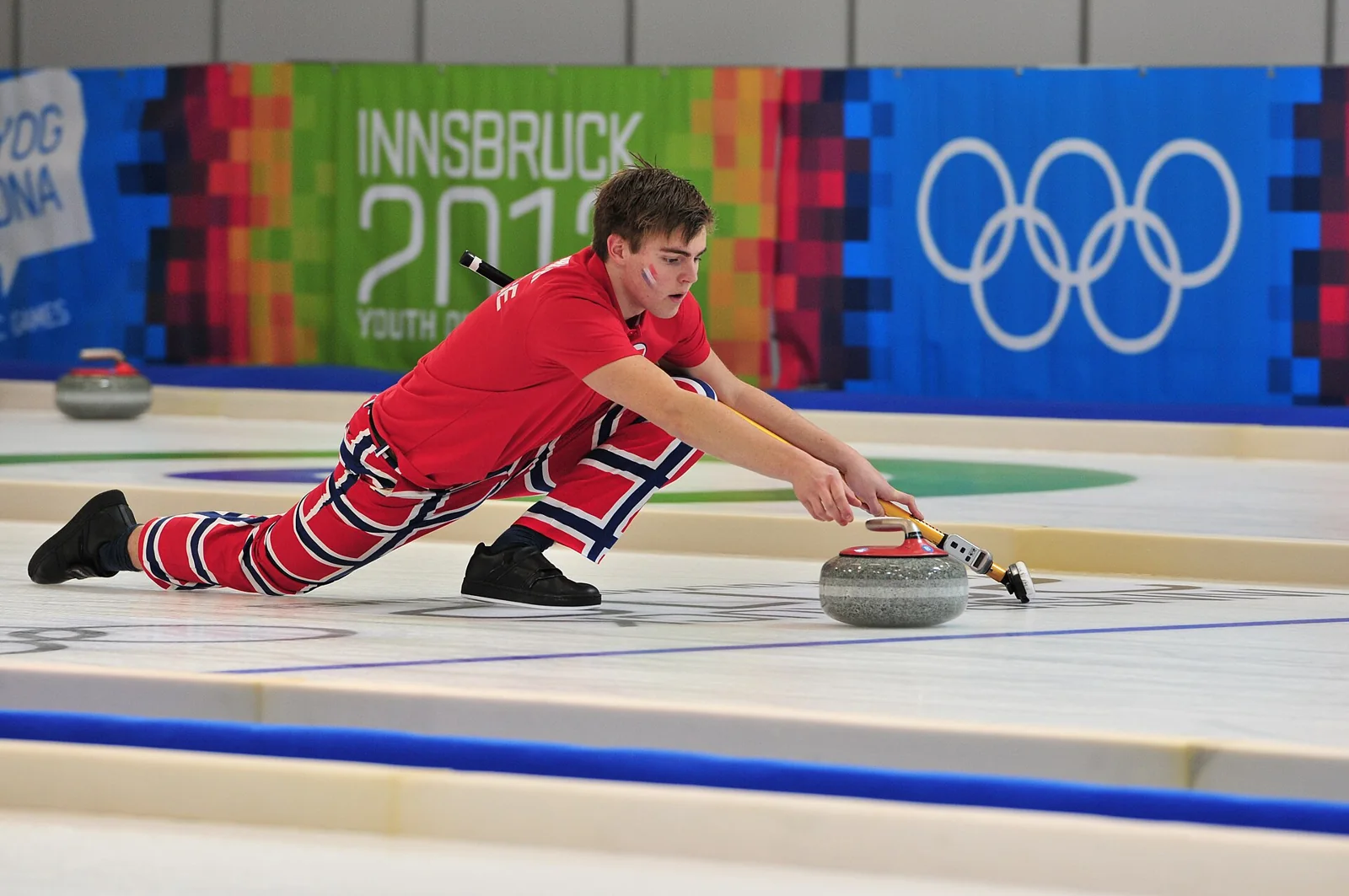 Un jugador de curling interviene junto a las piedras sobre el hielo.