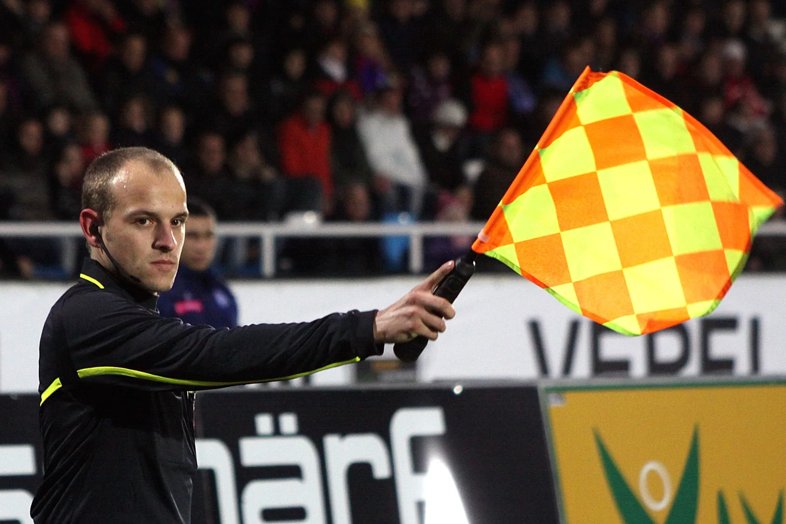 Un árbitro asistente levanta su banderín en un partido de fútbol.