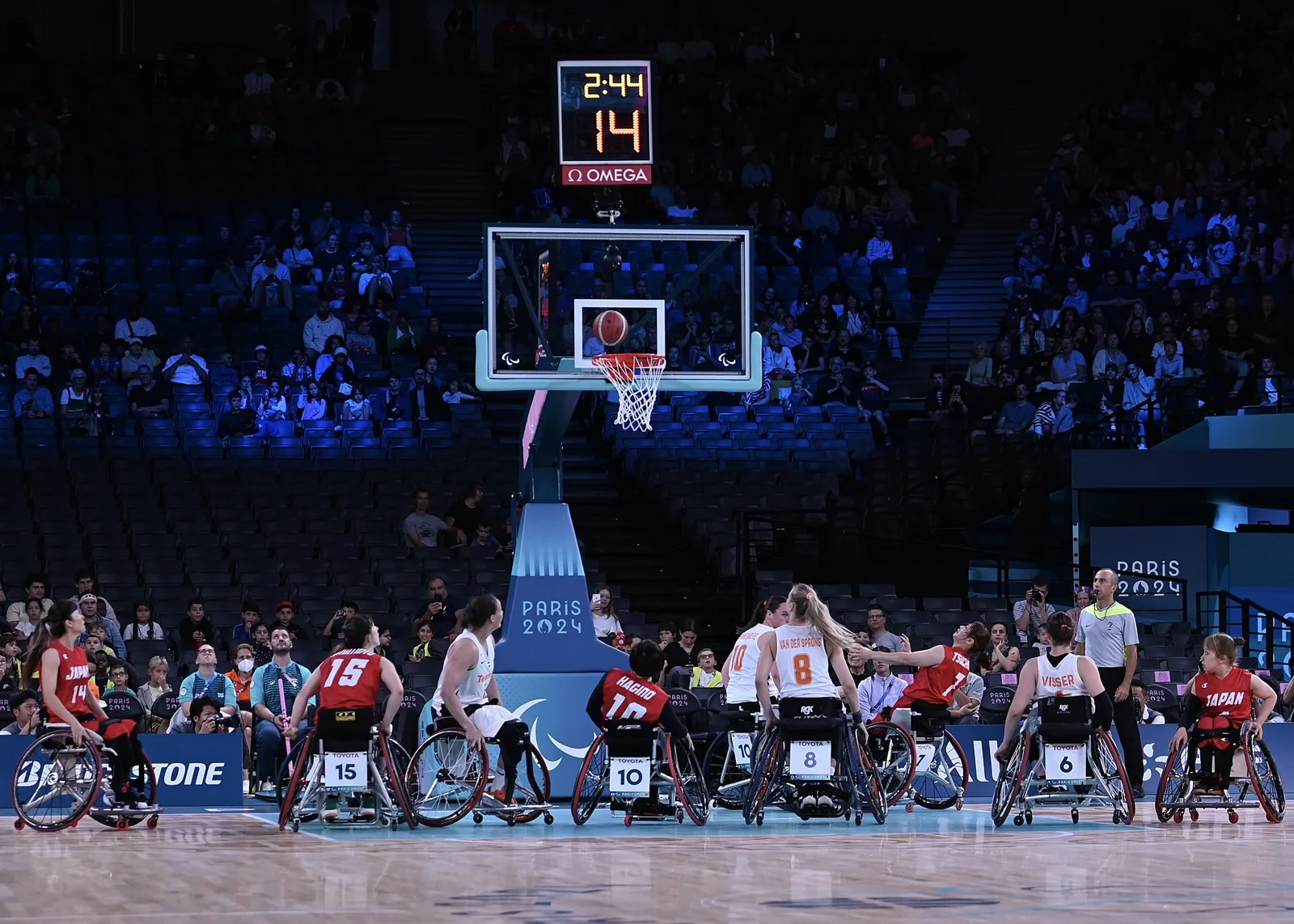 Jugadoras de baloncesto en silla disputan una acción cerca de la canasta.