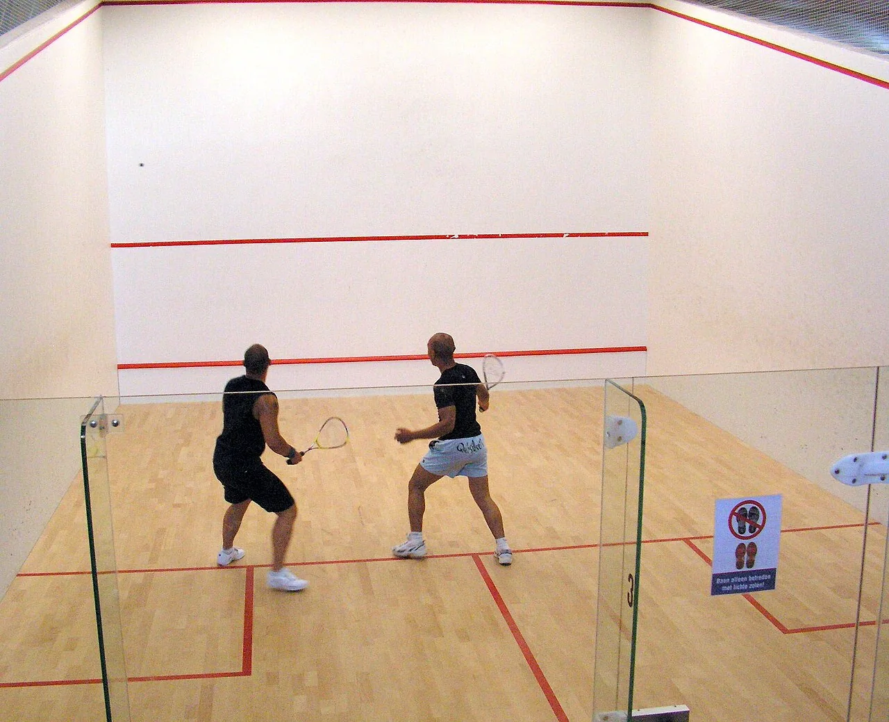 Dos jugadores de squash comparten la pista durante un intercambio.