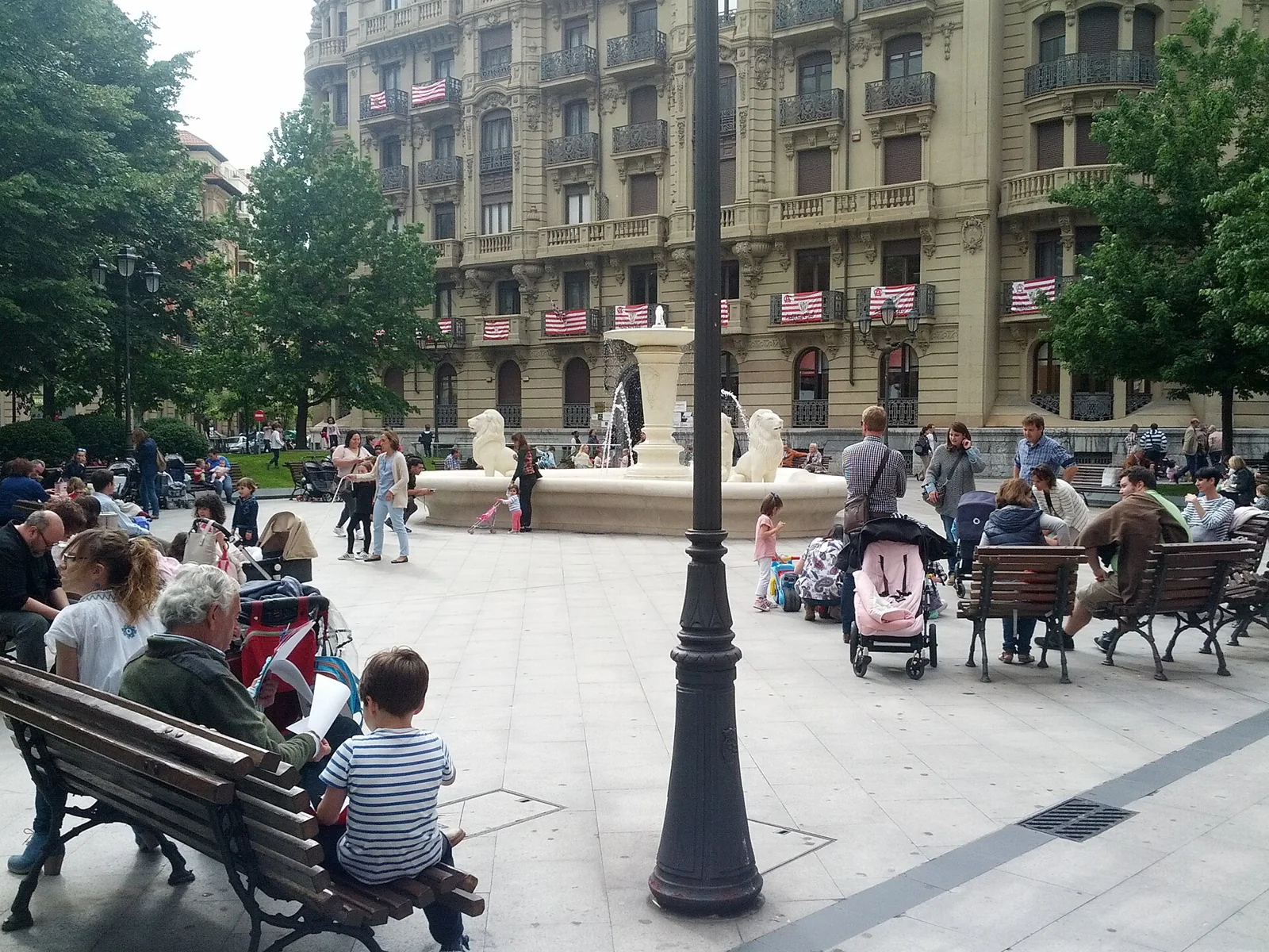 Personas sentadas junto a una fuente en una plaza.