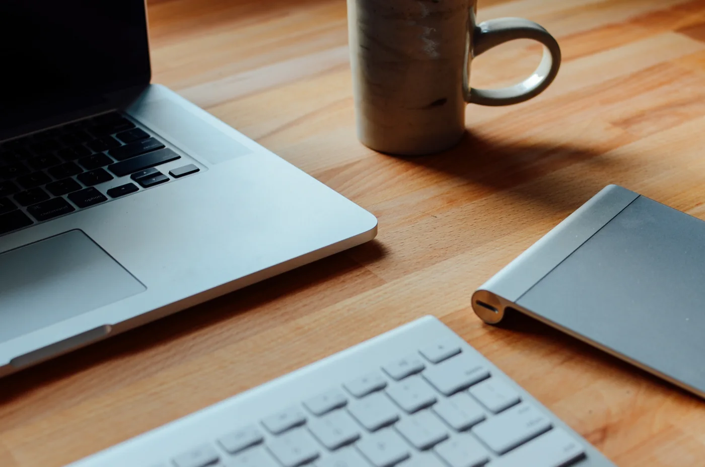 Portátil, teclado y taza sobre una mesa de madera